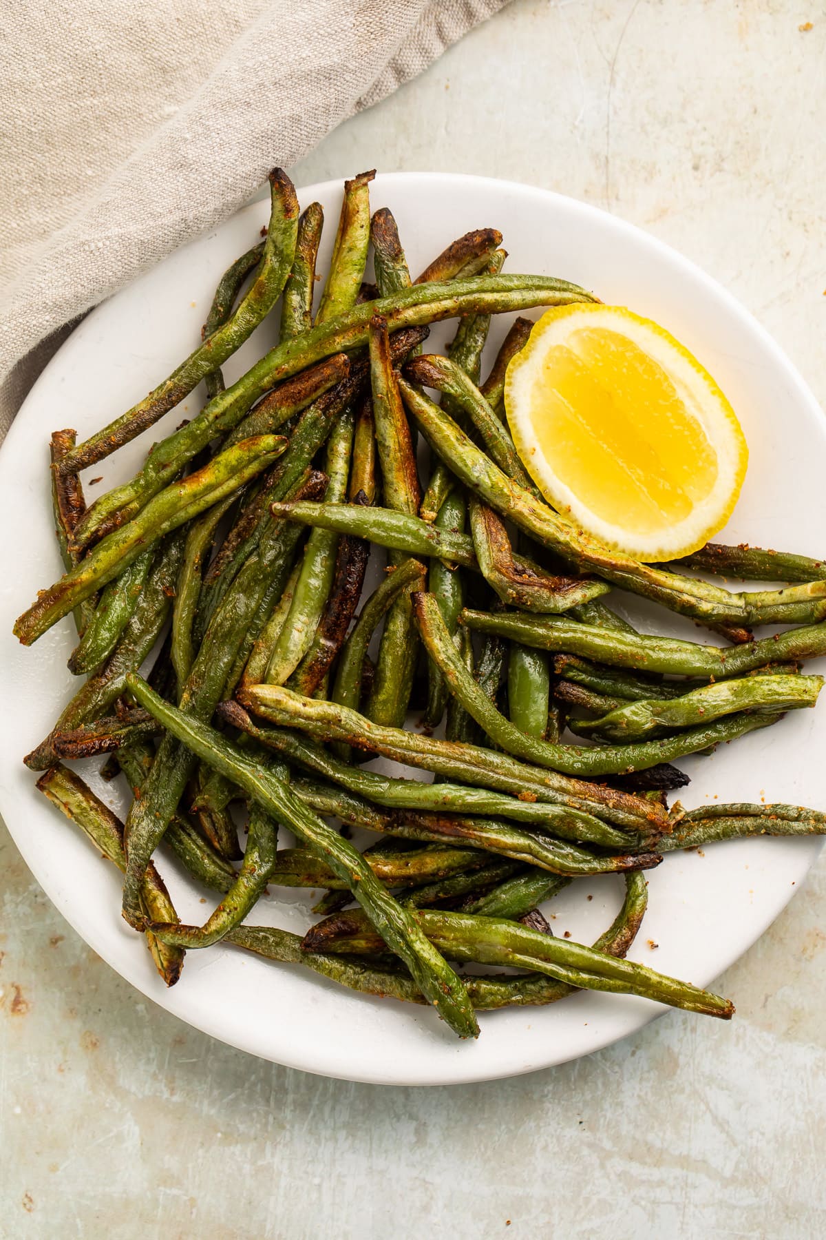 Zoomed out photo of air fryer frozen green beans on a white plate.