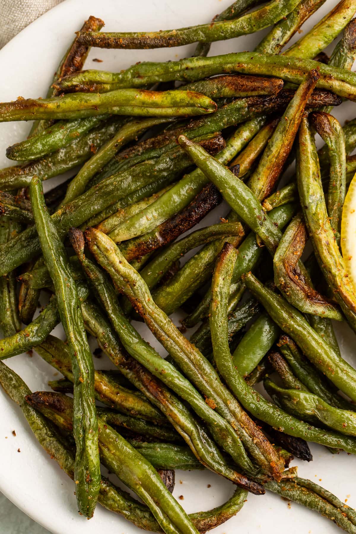 Close-up of air fryer frozen green beans on a white plate.