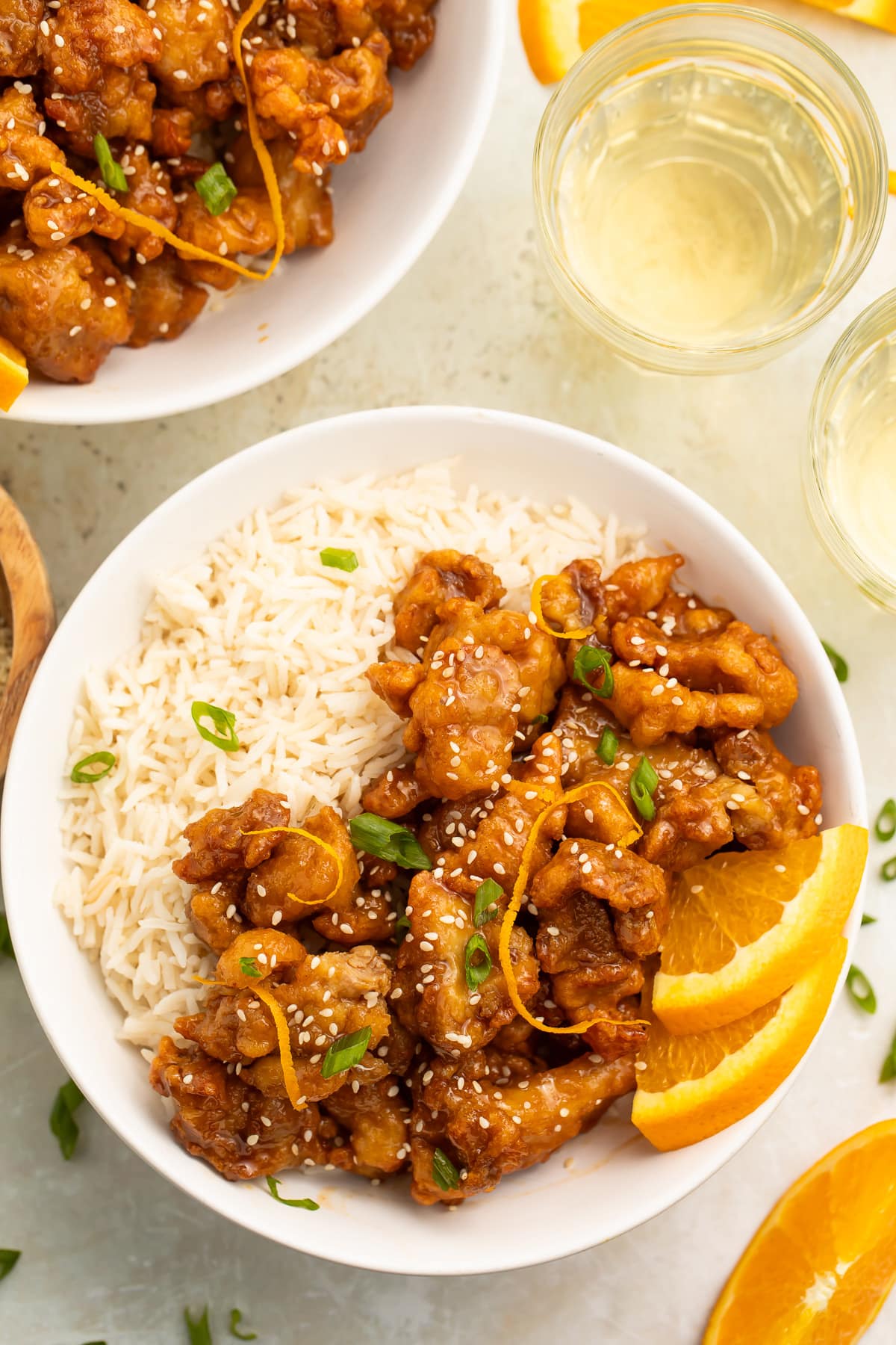 Zoomed-out overhead photo of a bowl of Trader Joe's orange chicken cooked in the air fryer served with white rice and orange wedges for garnish.
