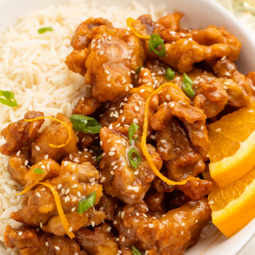Close-up of Trader Joe's orange chicken cooked in the air fryer and served with white rice and orange wedges for garnish.