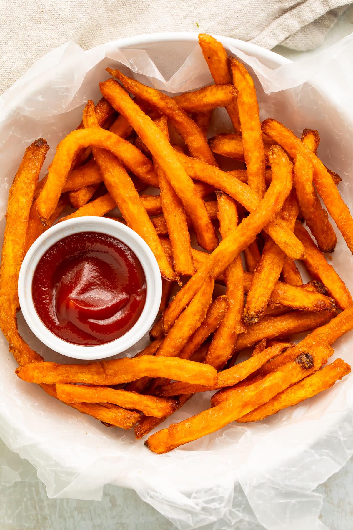 A bowl of air fryer frozen sweet potato fries with a ramekin of ketchup.