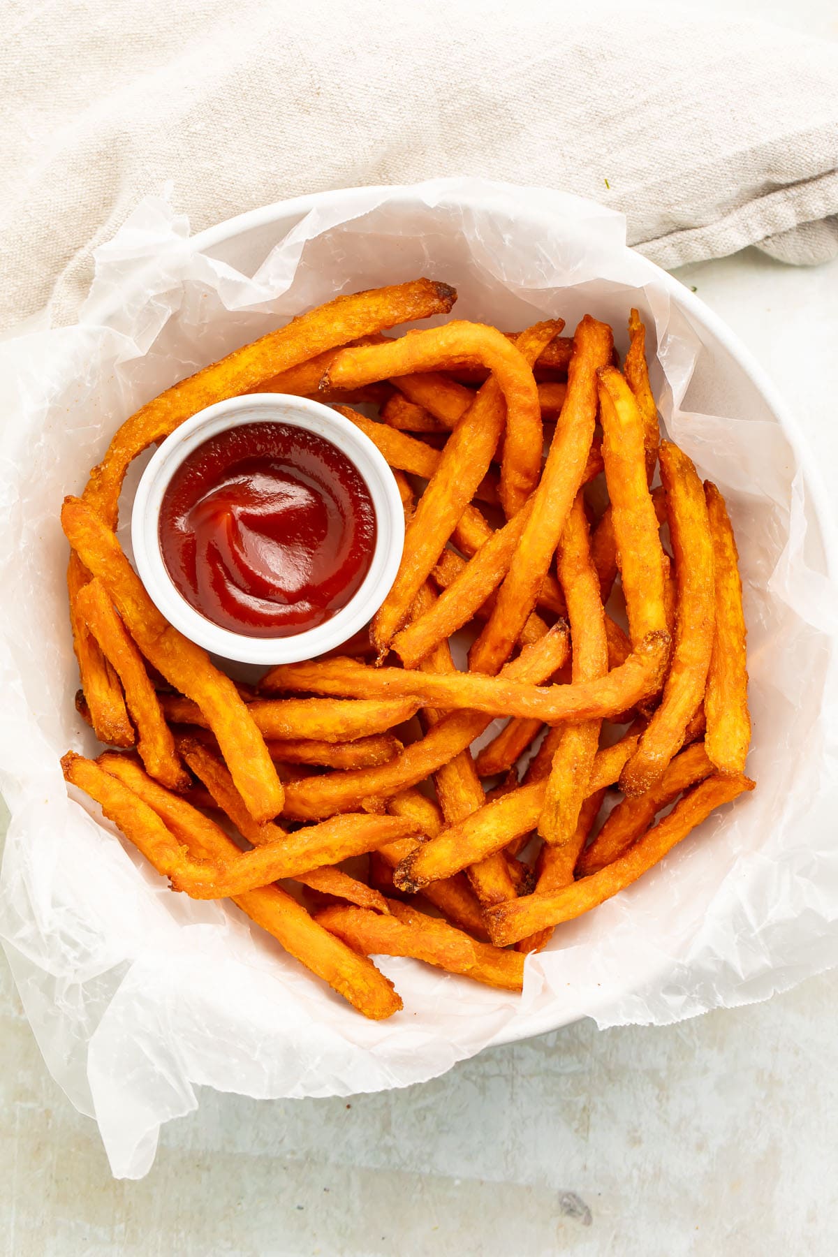 A bowl of air fryer frozen sweet potato fries with a ramekin of ketchup.