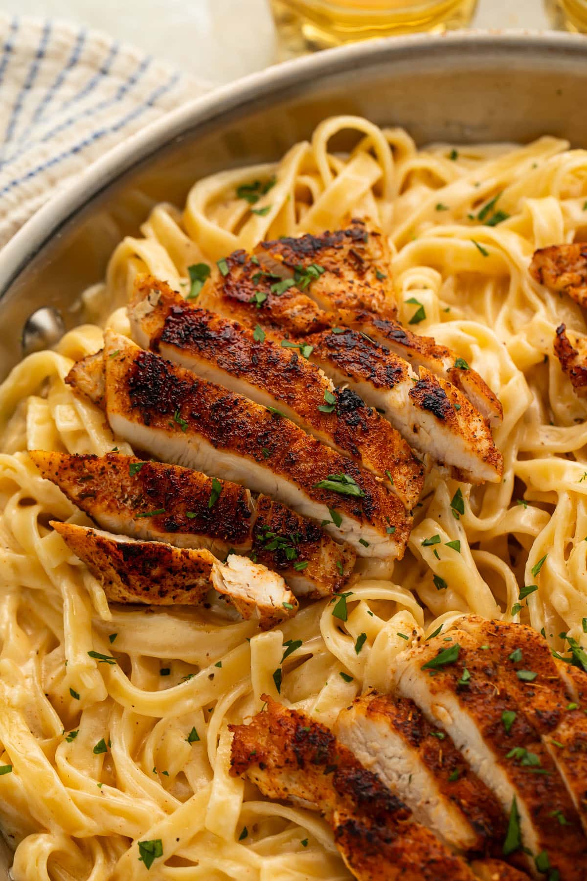 A skillet of fettucine pasta with alfredo sauce and blackened chicken breasts.