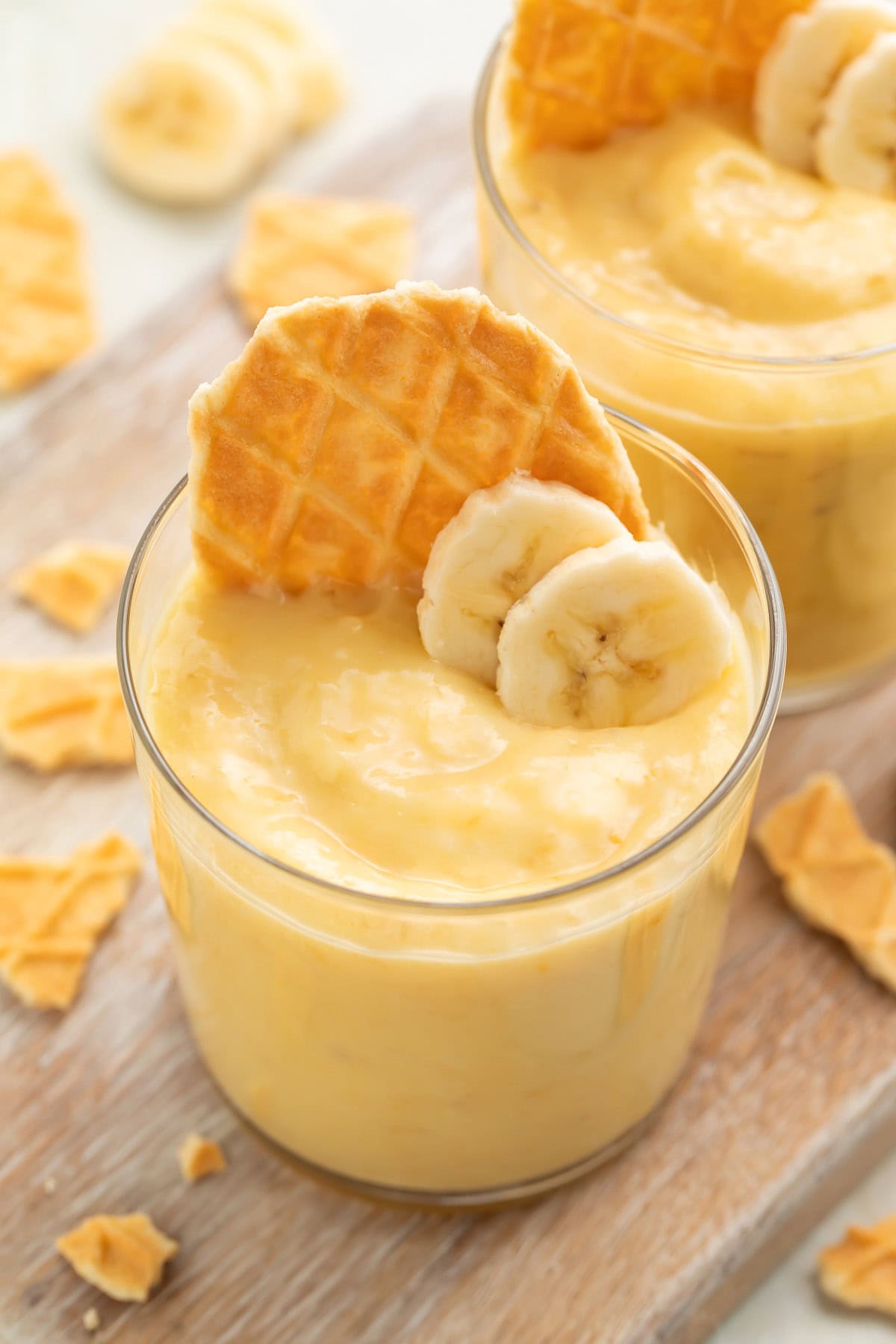 A small glass cup holding banana custard with a waffle cone cookie and two slices of banana on top for garnish.