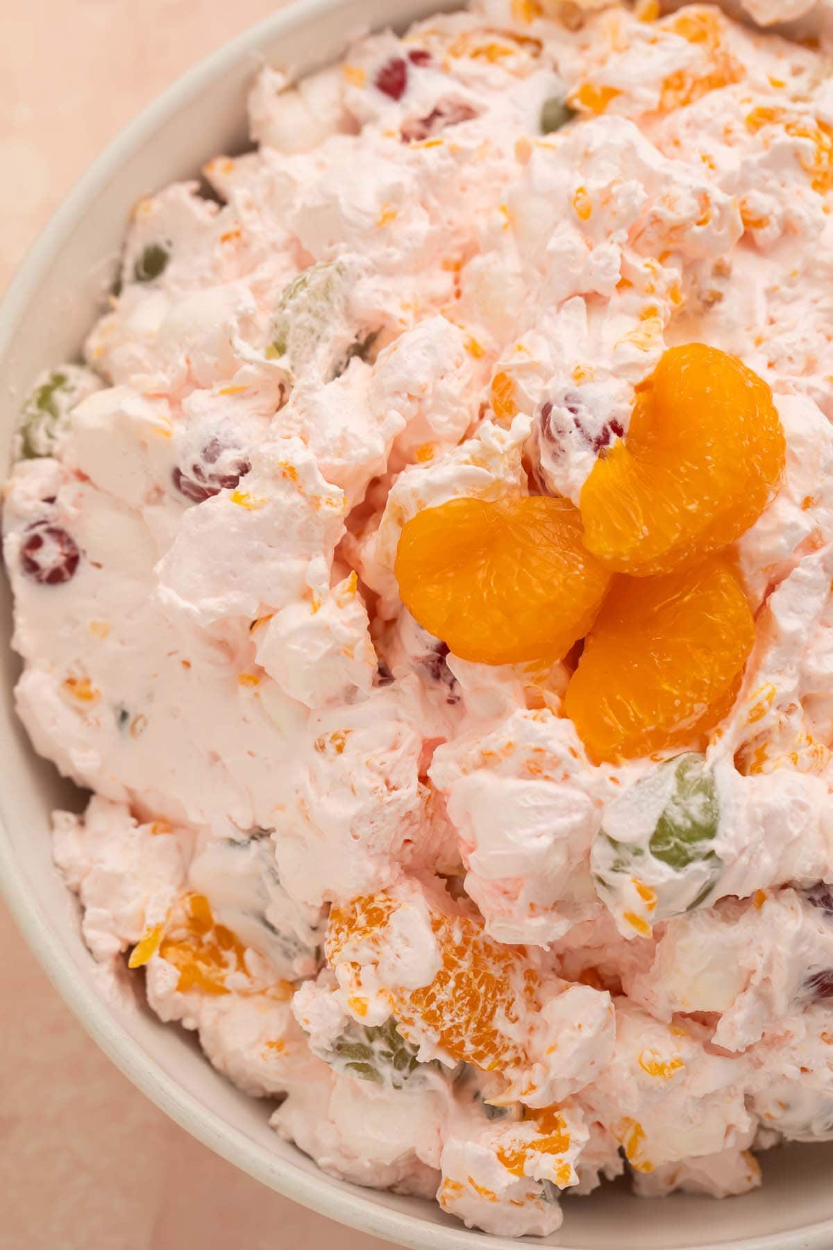 A large bowl of fruit salad made with Cool Whip, maraschino cherries, mandarin oranges, seedless grapes, and marshmallows.