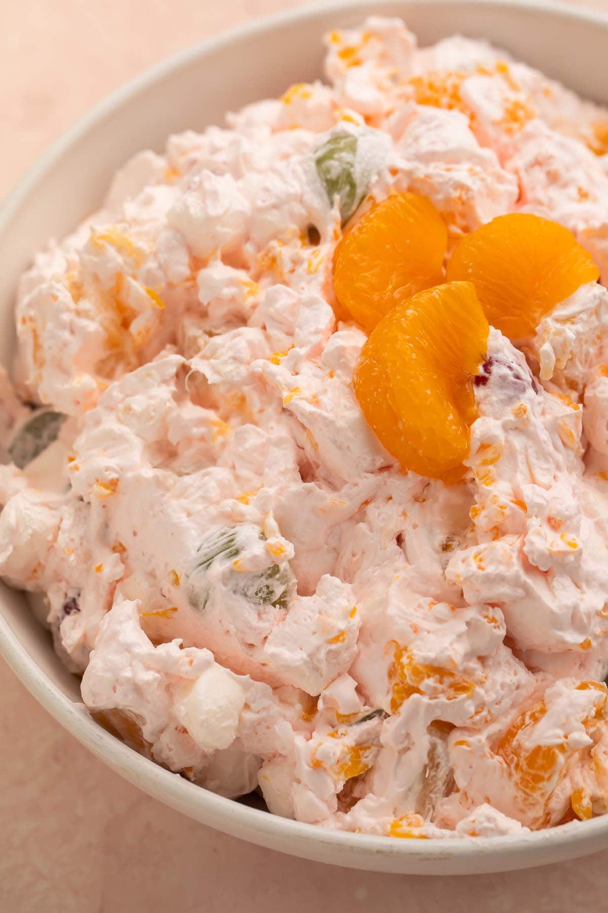 A large bowl of fruit salad made with Cool Whip, maraschino cherries, mandarin oranges, seedless grapes, and marshmallows.
