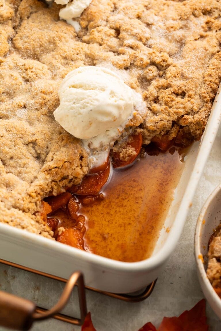 A baking dish of sweet potato cobbler, with a large scoop removed from the corner of the dish, revealing the sweet potato slices beneath the cobbler topping.