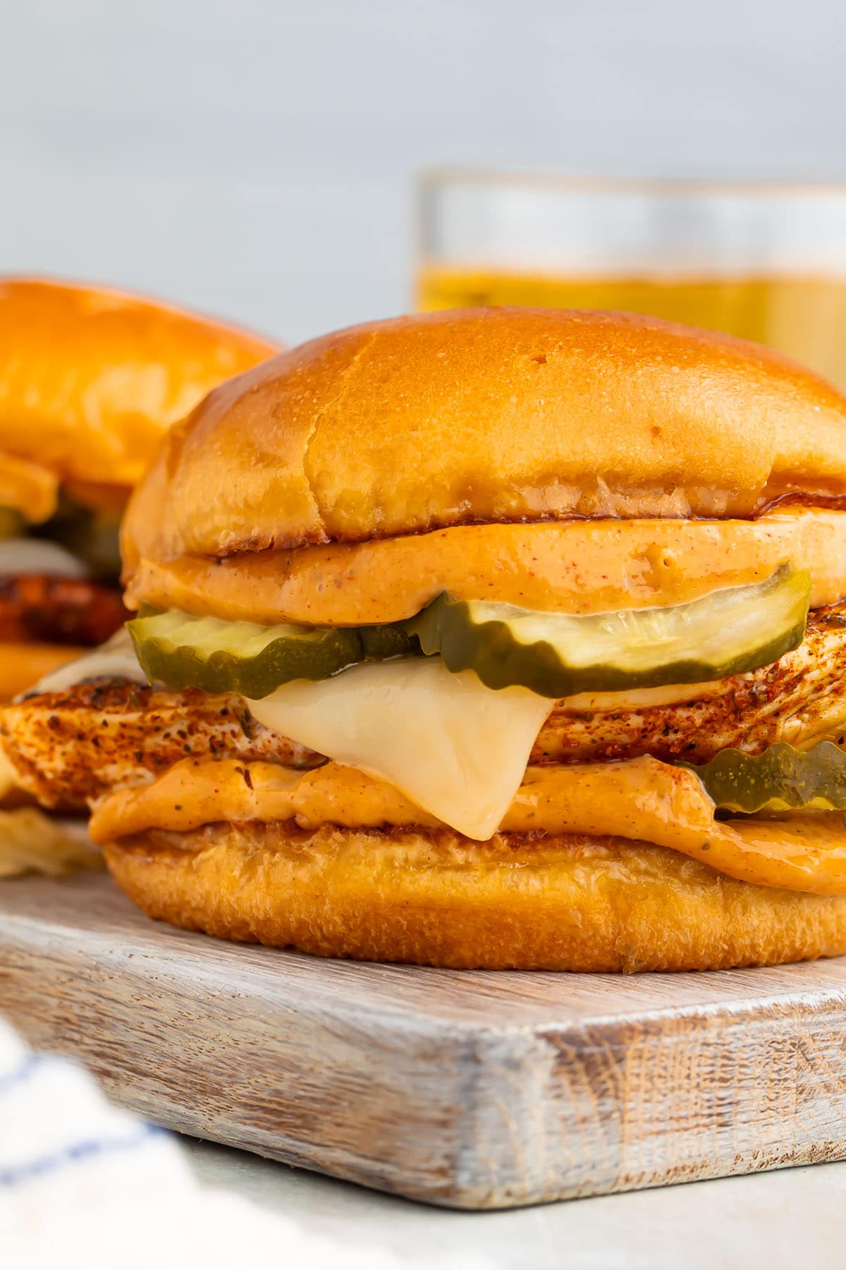 Close-up of a blackened chicken sandwich with pickles and cheese resting on a wooden board.