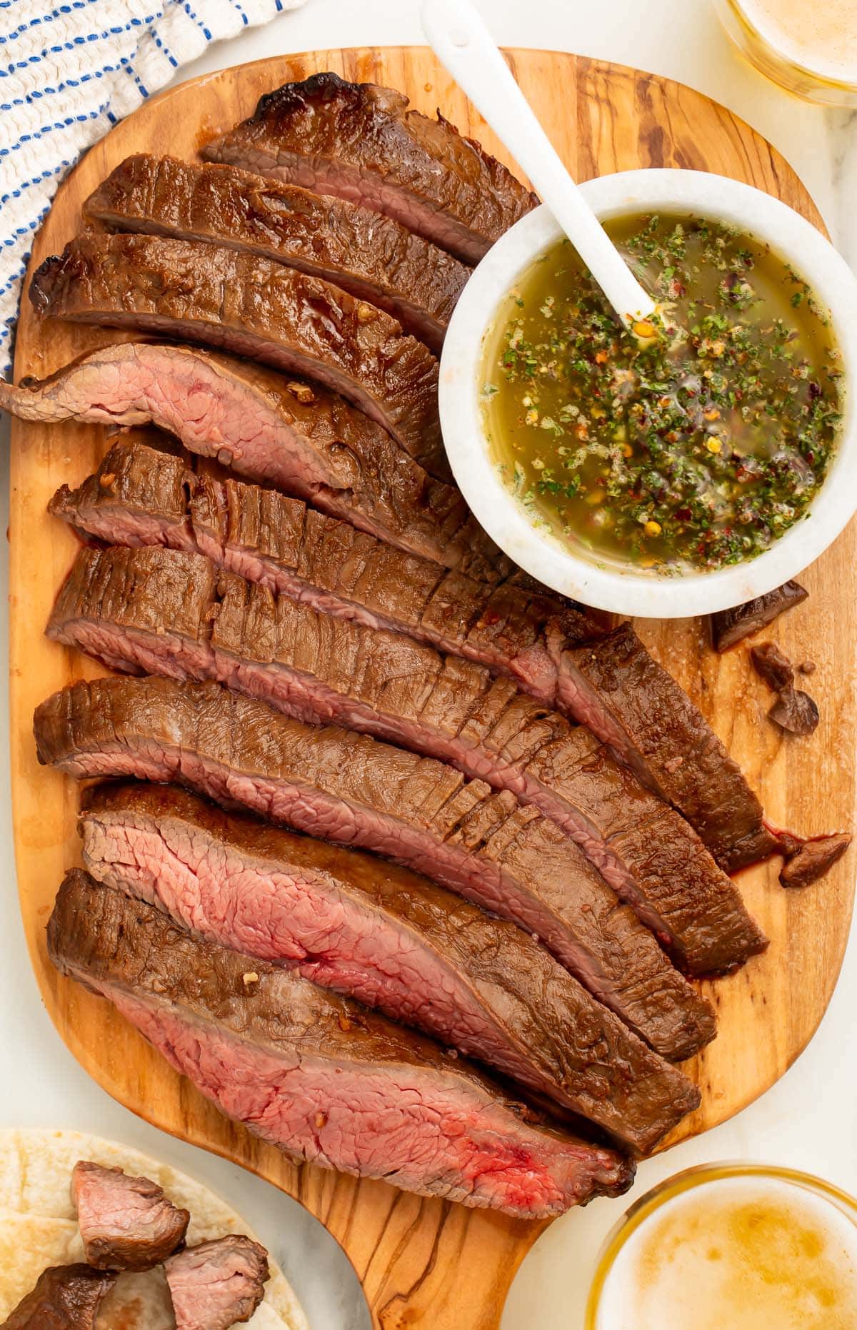 Air fryer flank steak, sliced into strips and arranged on a wooden serving board next to a bowl of chimichurri sauce.