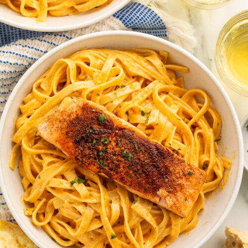 Two bowls of creamy pasta topped with spiced salmon fillets.