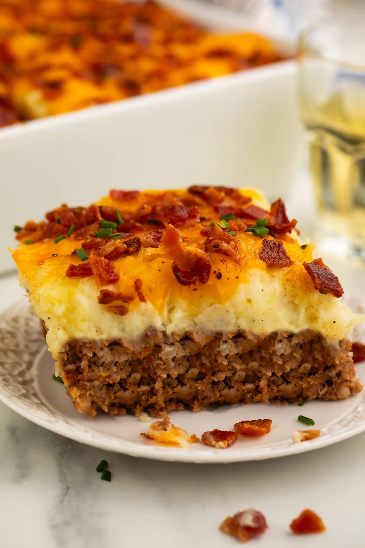 Slice of meatloaf casserole on a white plate with the main casserole just visible in the background.