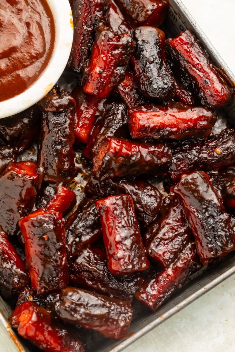 Close up of a tray of hot dog burnt ends with a white pot of sauce just visible off to the side.