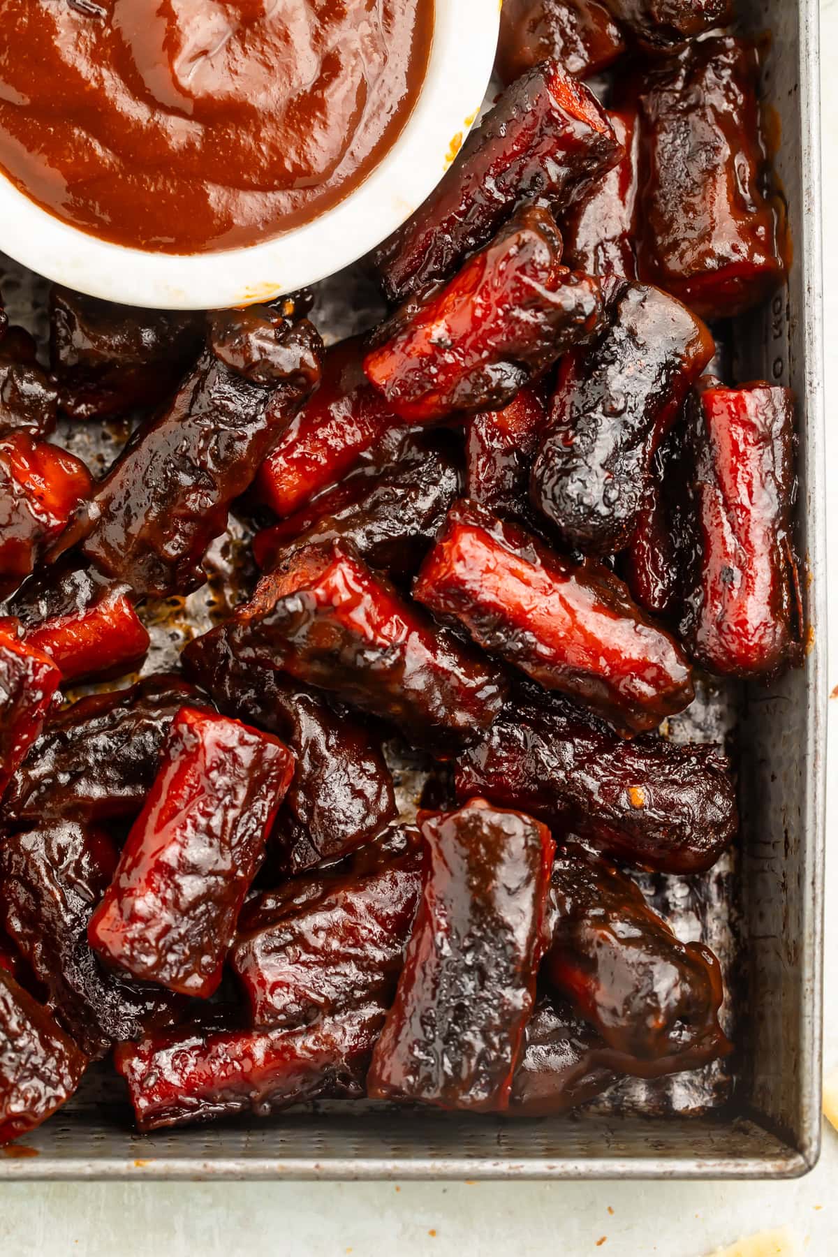 Close up of hotdog burnt ends in a metal tray with a small pot of barbecue sauce.
