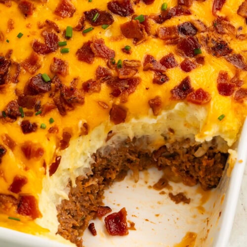 Bacon, cheese and chive-topped mashed potato meatloaf casserole with a spoonful taken out of the corner to show the meat layer underneath.