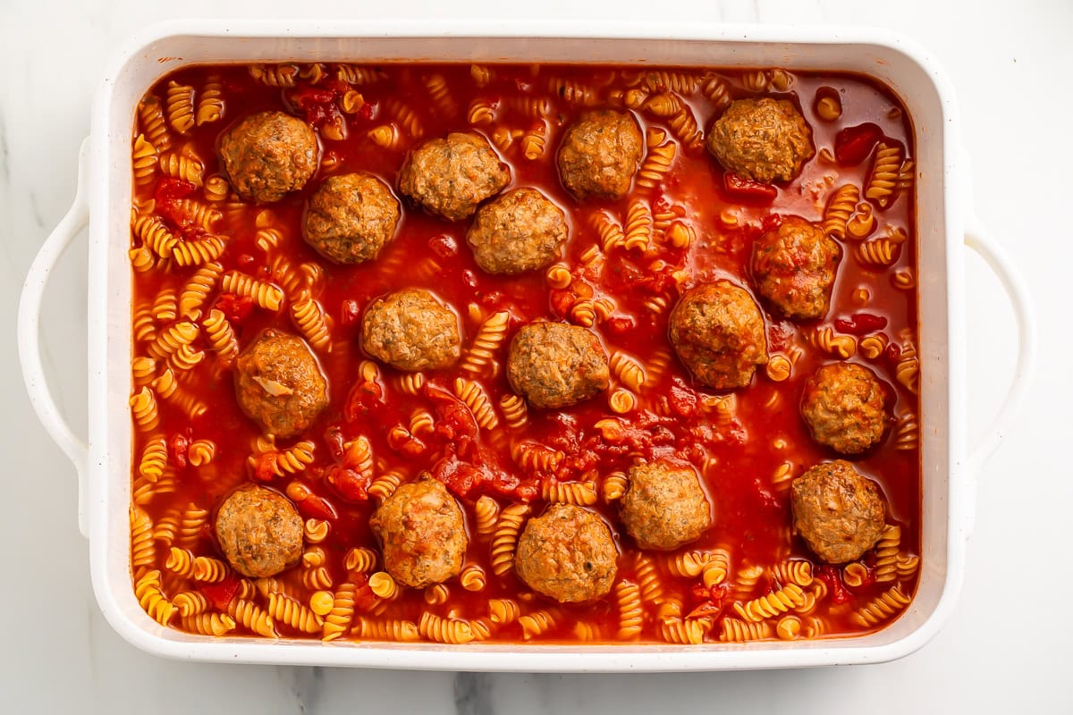 Uncooked dump and bake meatball casserole in a white ceramic baking dish. 