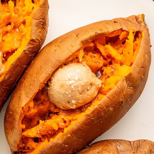 Close up of 3 split sweet potatoes filled with a scoop of cinnamon honey butter and sprinkled with flaky sea salt.