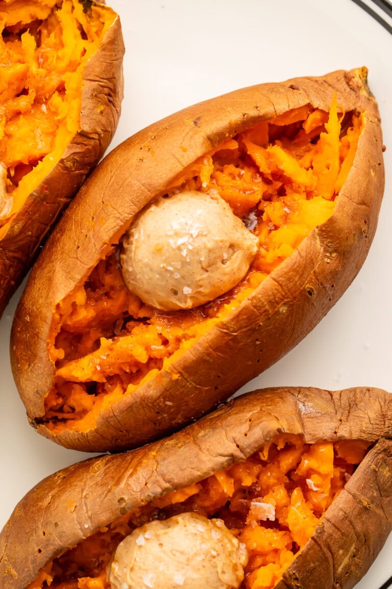 Close up of 3 split sweet potatoes filled with a scoop of cinnamon honey butter and sprinkled with flaky sea salt.