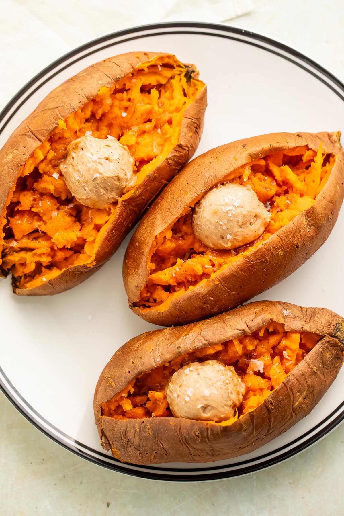 Smoked sweet potatoes on a white plate with a black rim, split open with scoops of compound butter nestled inside each one. 