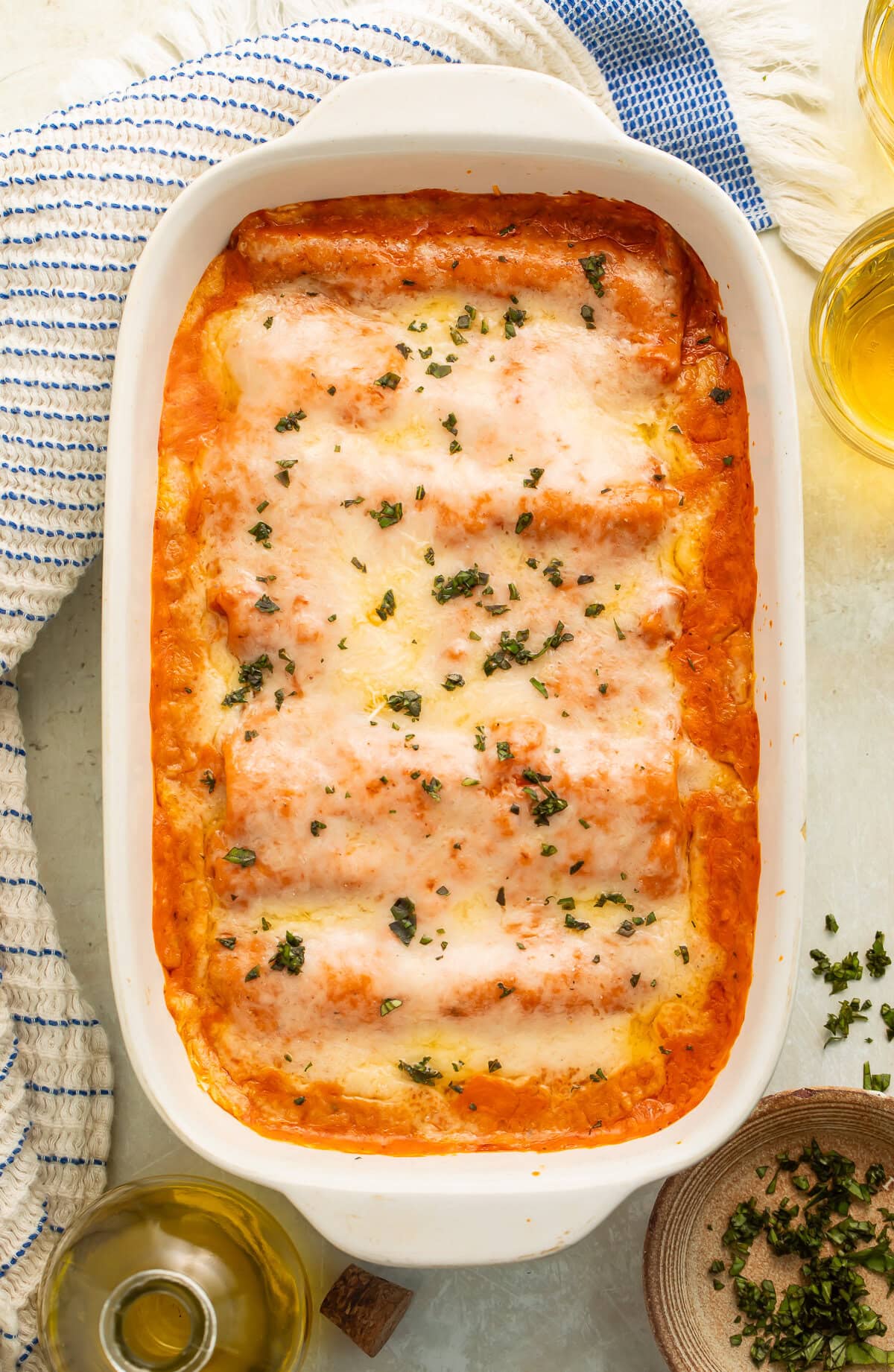 Overhead shot of baked chicken cannelloni with glasses of beer and a bottle of olive oil visible off to the side.