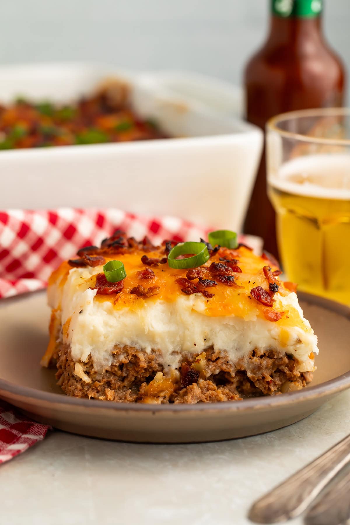 A slice of casserole pictured side-on to show the beef bottom, mashed potato top and cheesy bacon topping.