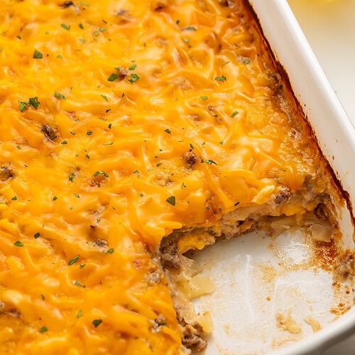 Close up of a hobo casserole baked in a white baking dish with a portion removed from the corner.
