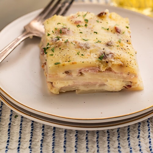 Slice of potato lasagna on a white plate to show the layers of potato, ham and cheese.