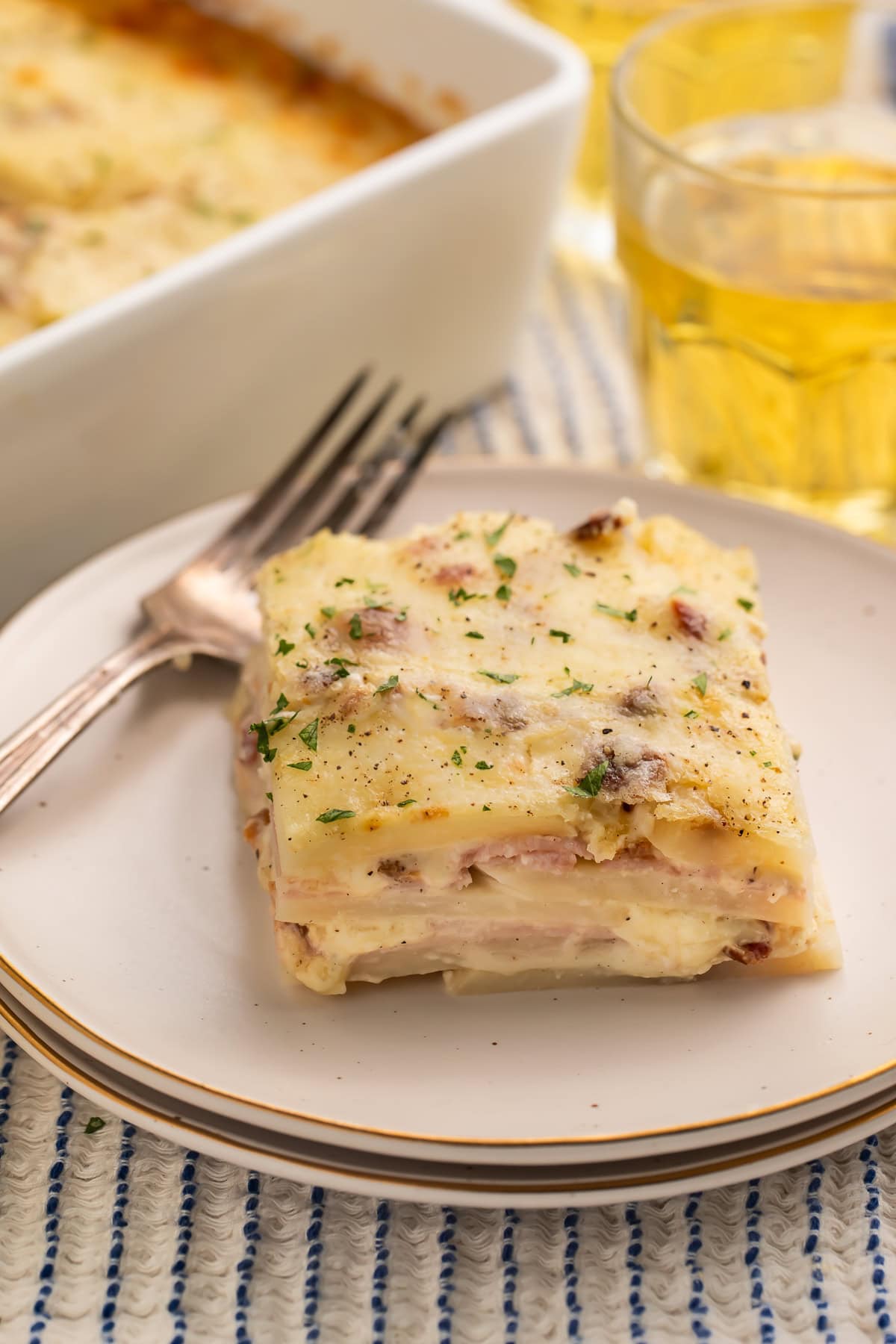 Slice of potato lasagna on a white plate to show the layers of potato, ham and cheese.