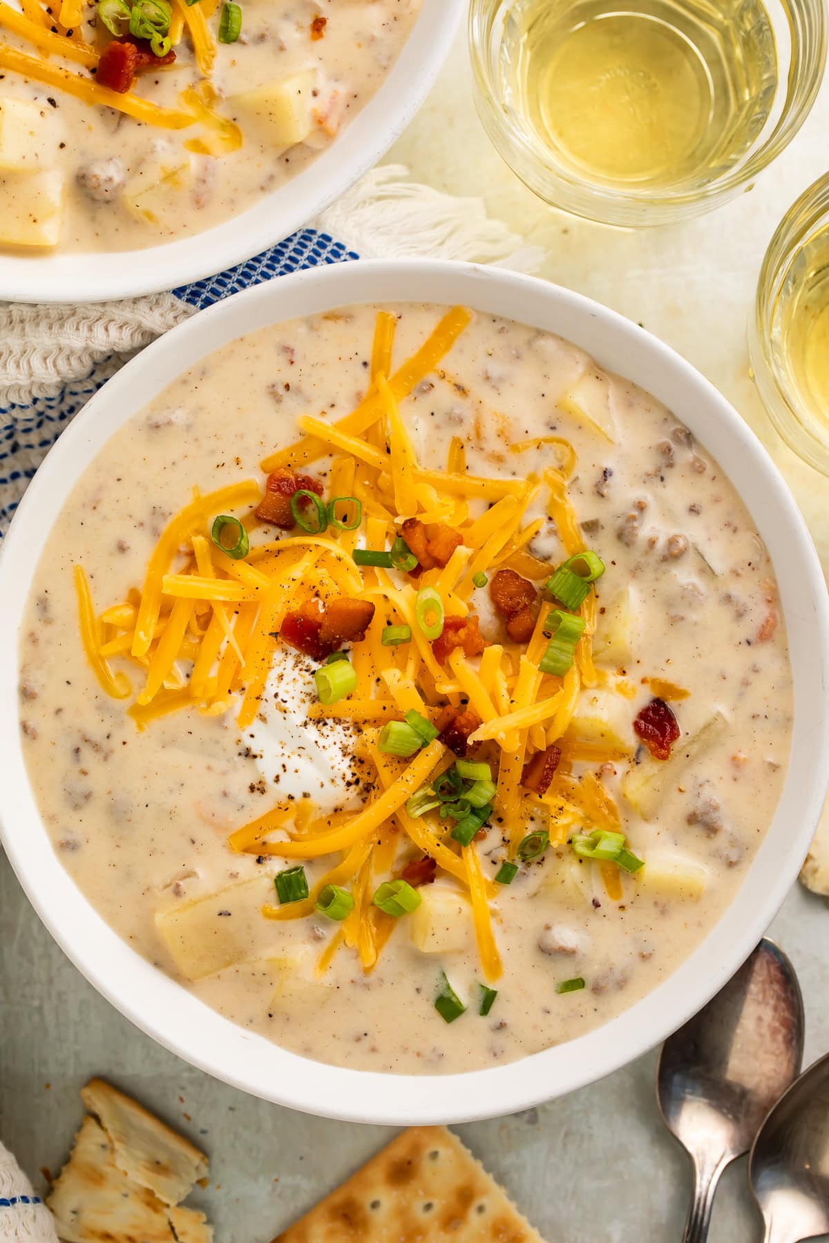 Creamy Hamburger Potato Soup in white bowls with shredded cheddar, green onions, and bacon bits. The picture is from overhead.