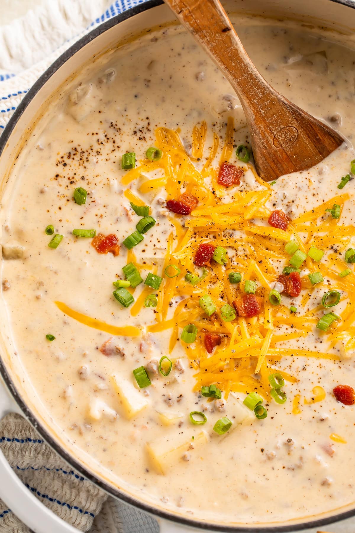 Creamy hamburger soup with shredded cheddar, green onions, and black pepper in a Dutch oven.
