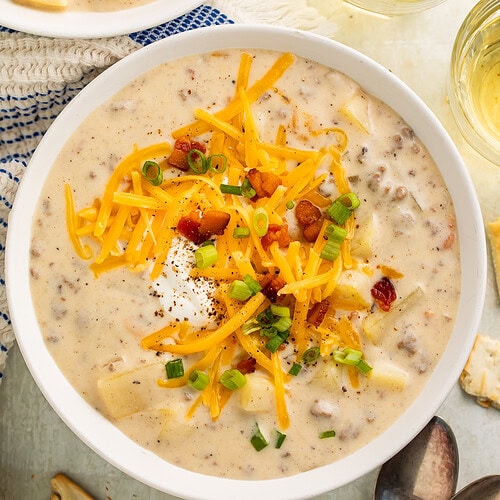 Two bowls of creamy soup topped with shredded cheese, sour cream, bacon bits and green onions.