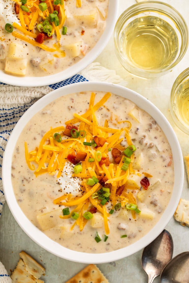 Two bowls of creamy soup topped with shredded cheese, sour cream, bacon bits and green onions.