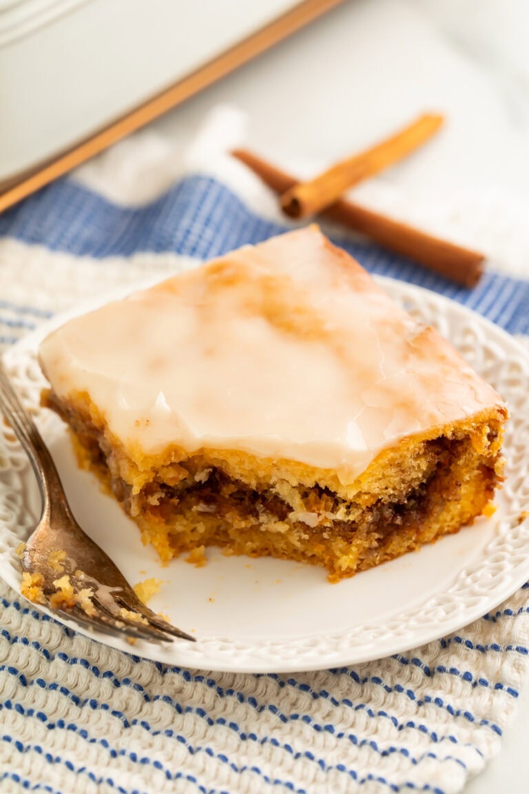 Slice of glazed honey bun cake on a plate showing the cinnamon swirl through the middle.