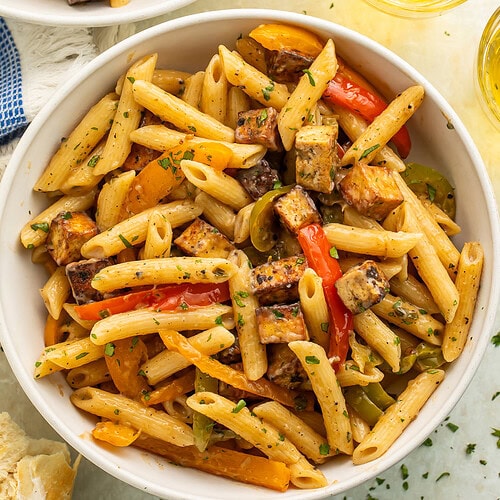 Two white bowls of vegan rasta pasta with glasses of wine pictured off to the side.