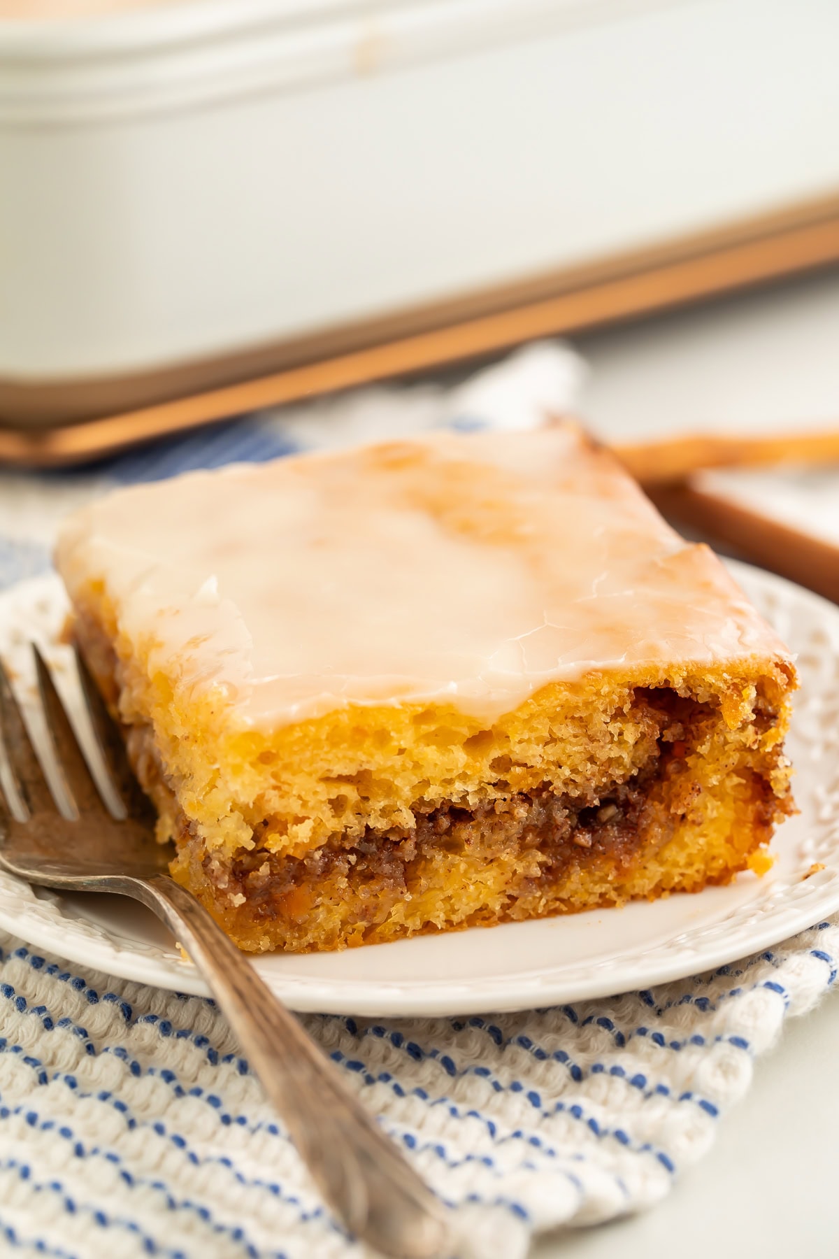 Slice of sweet potato honey bun cake with a thin glaze on a white plate with a fork.