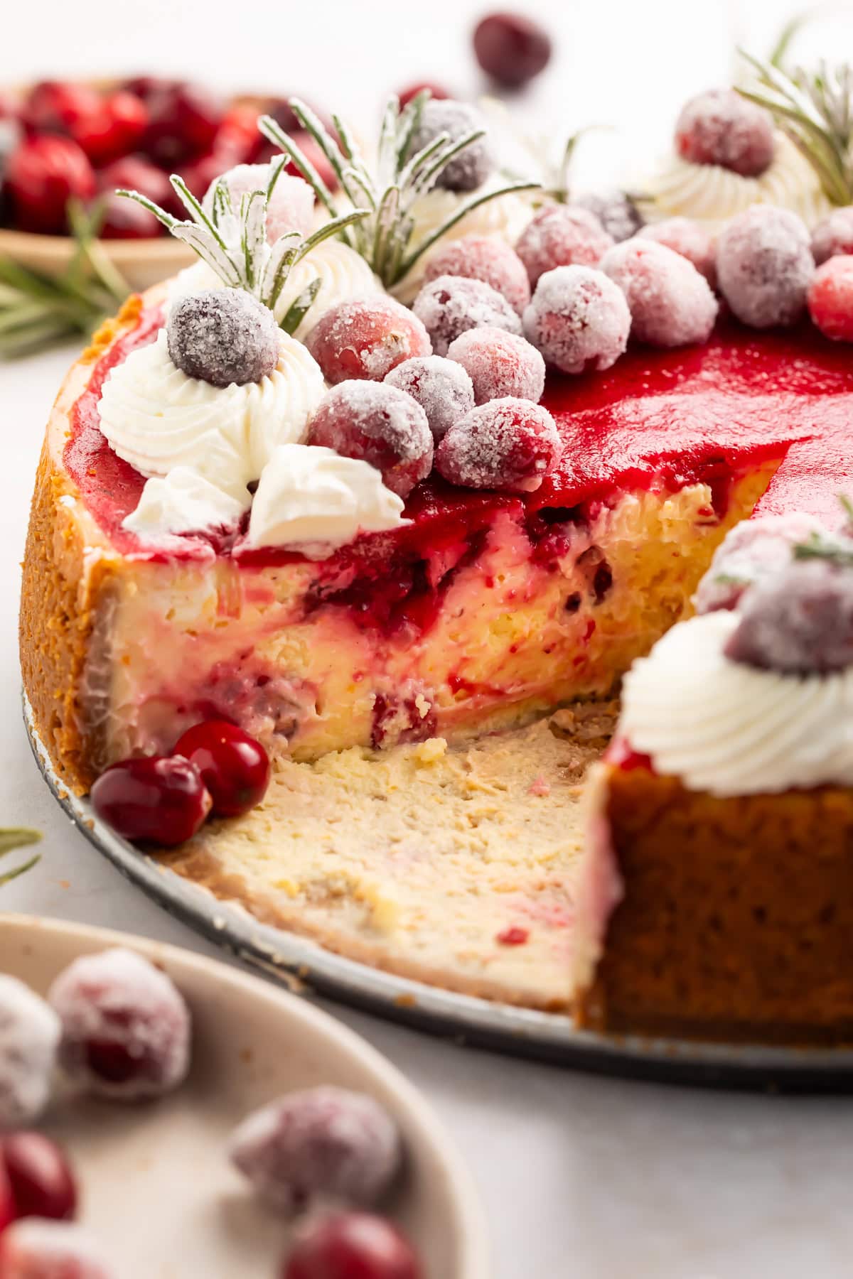 Side-on view of a cranberry cheesecake with a slice missing to show the creamy swirled middle.