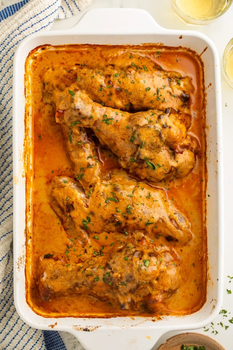 White baking dish of smothered turkey wings pictured top down with a glass of wine and blue and white kitchen towel visible just off to the side.