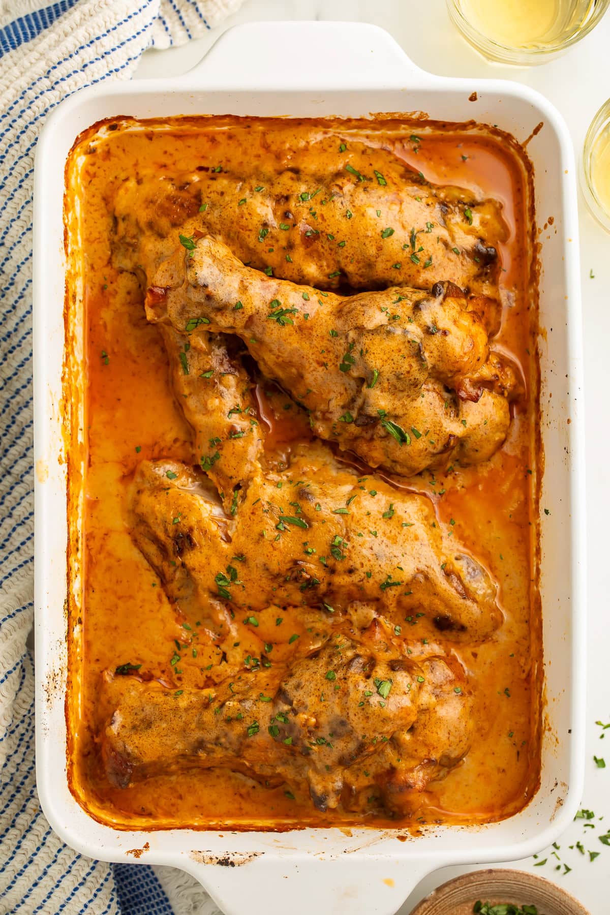 White baking dish of smothered turkey wings pictured top down with a glass of wine and blue and white kitchen towel visible just off to the side.