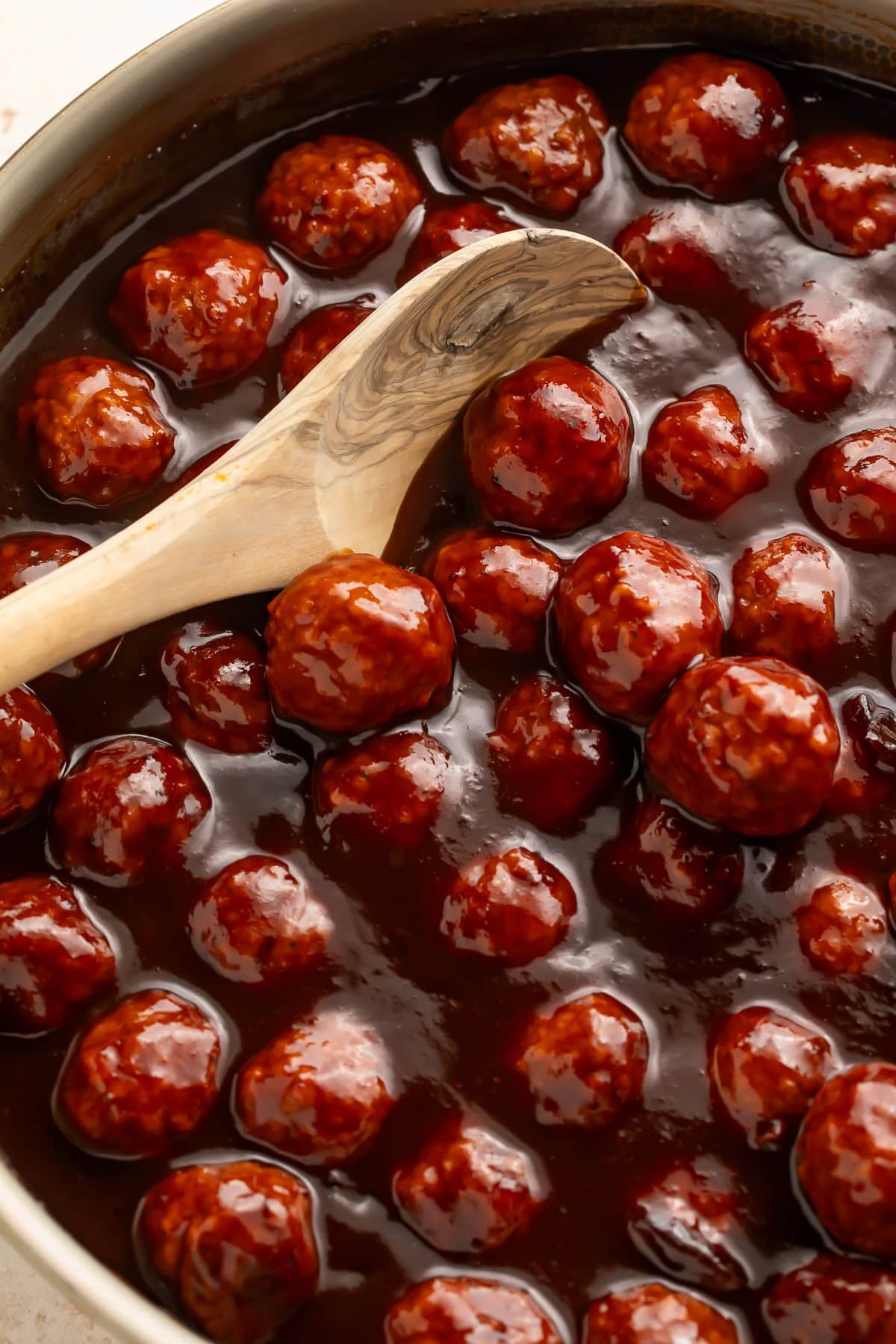 Cranberry glazed meatballs in a pot being stirred with a wooden spoon.