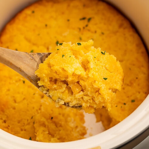 Wooden spoon lifting corn casserole out of the crockpot.
