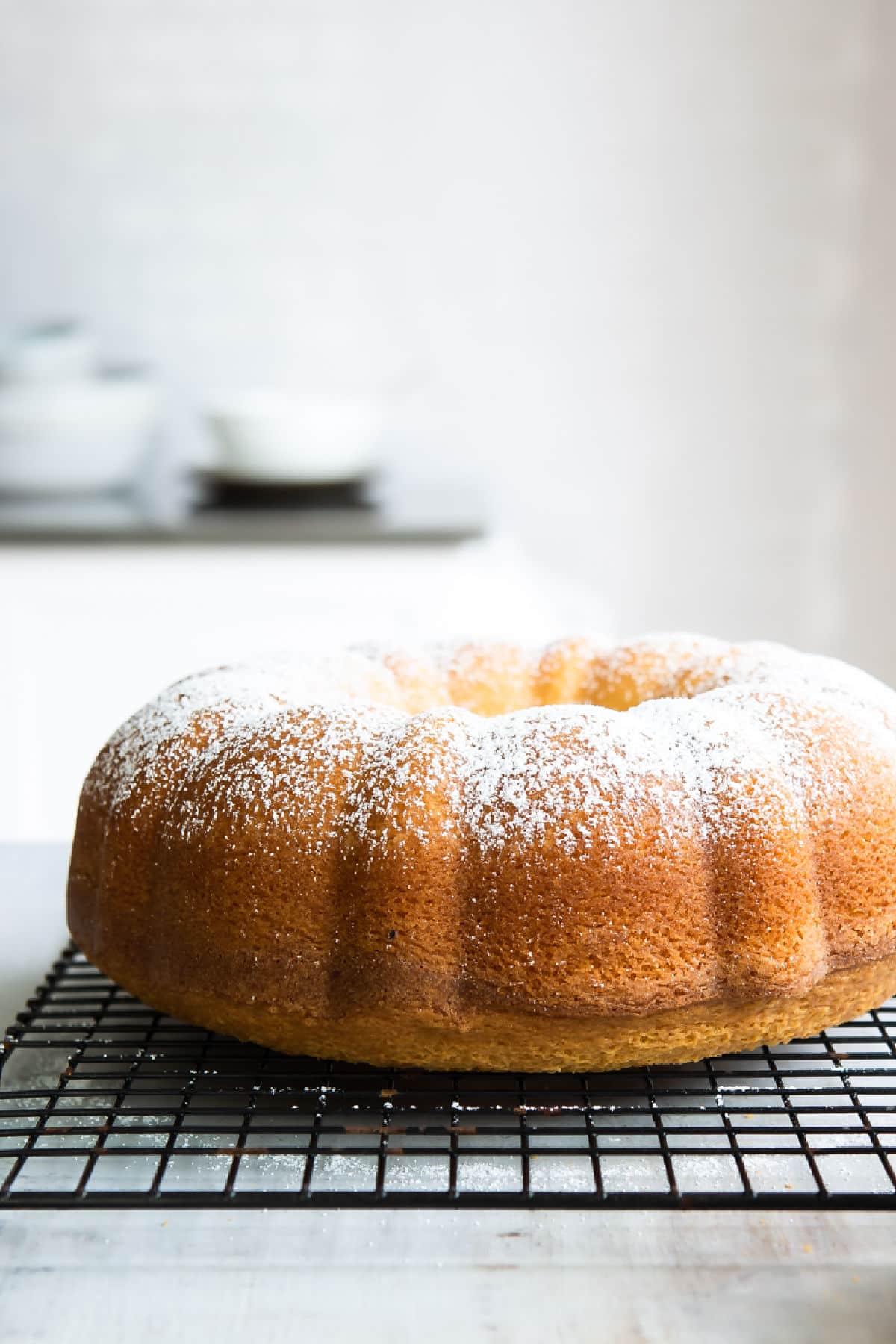 Hot milk bundt cake topped with powdered sugar on a wire rack.