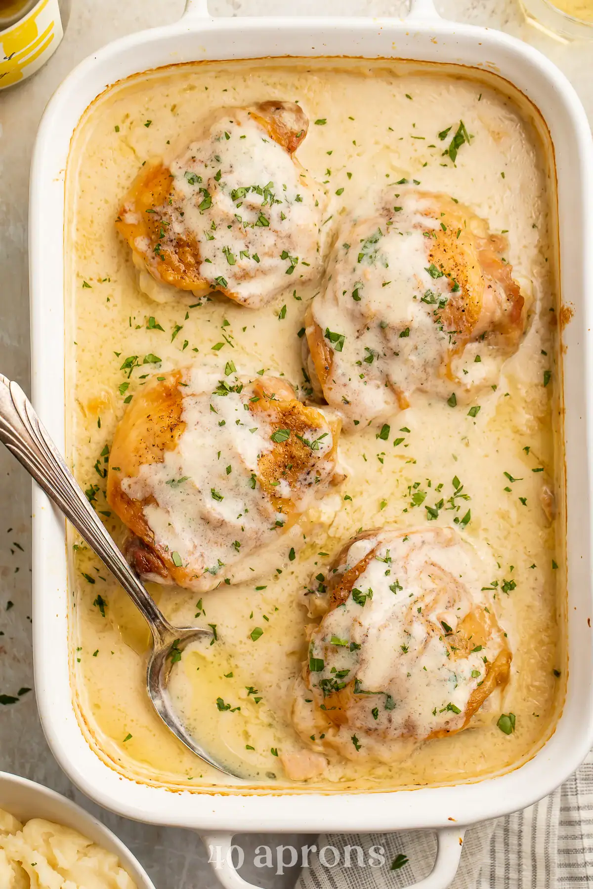 Overhead image of creamy chicken thighs in a white baking dish.