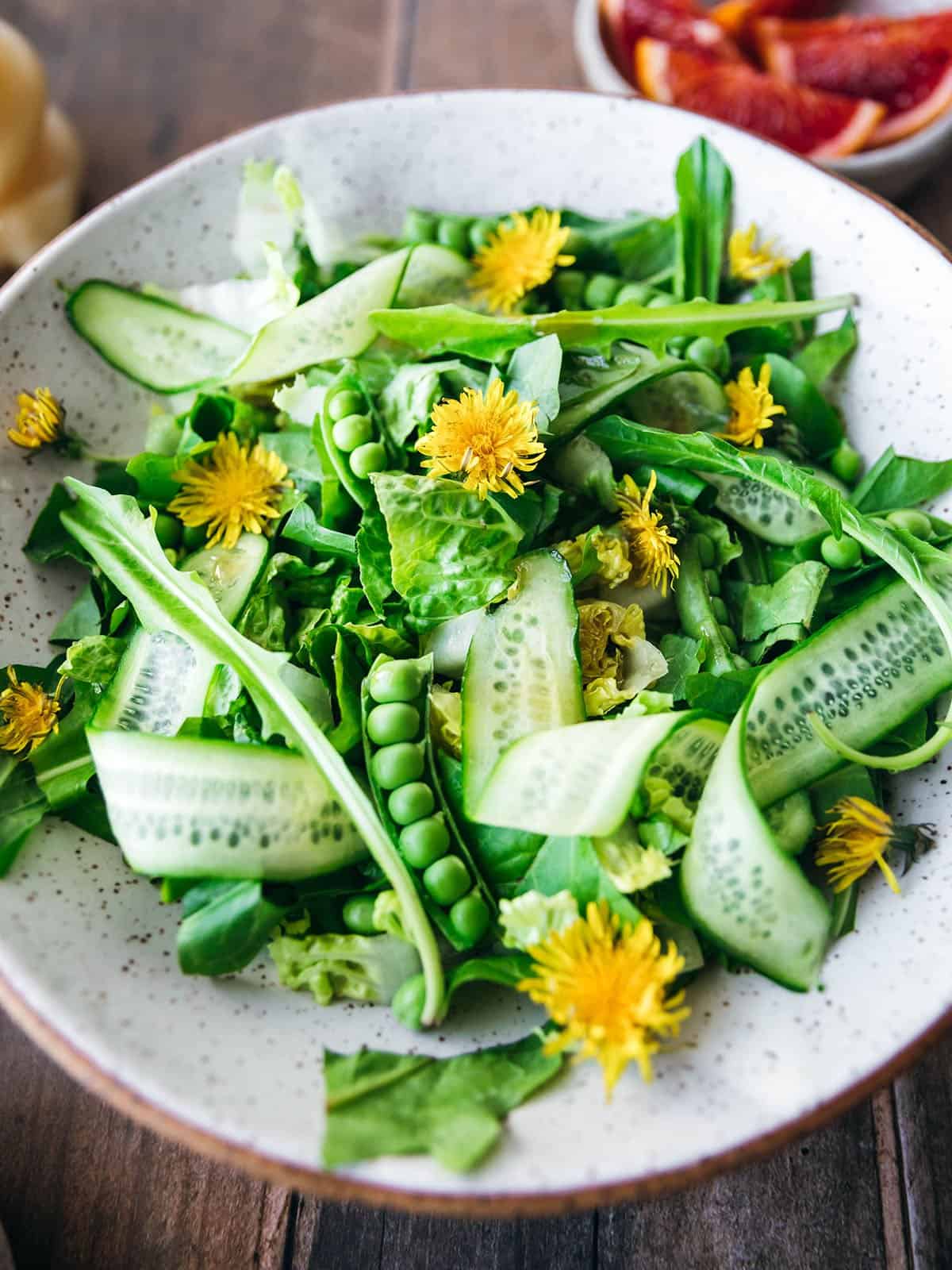 Close up of a dandelion leave salad with pea pots, shaved cucumber and dandelion flowers.