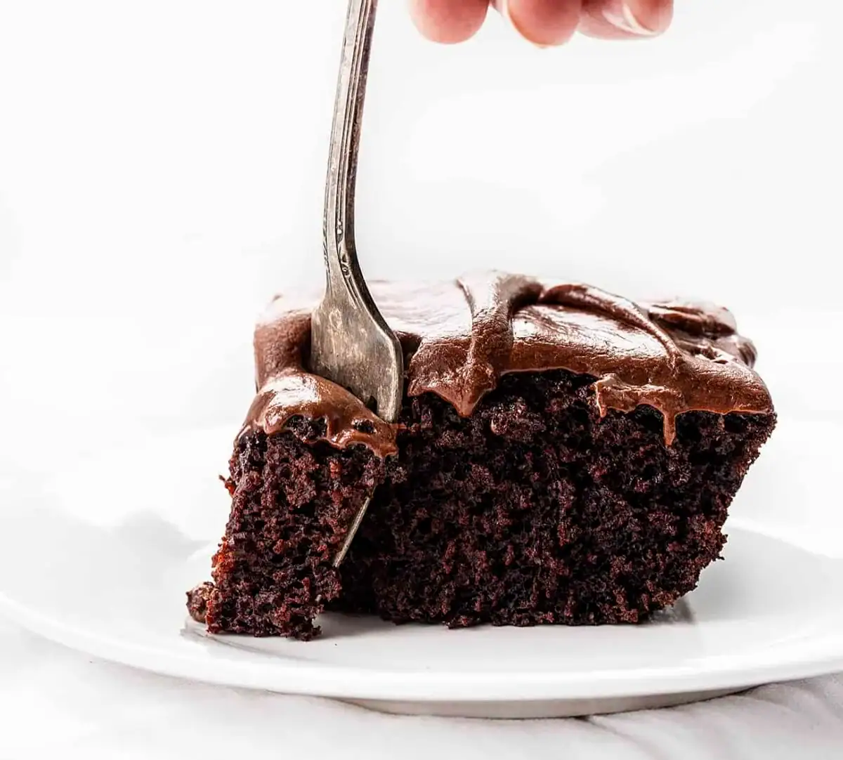Close up of a fork dipping into a slice of frosted chocolate cake.