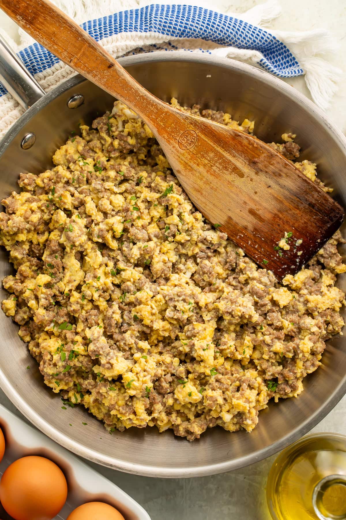 Overhead view of beef and eggs being stirred in a frying pan. There is a tray of eggs off to one side.