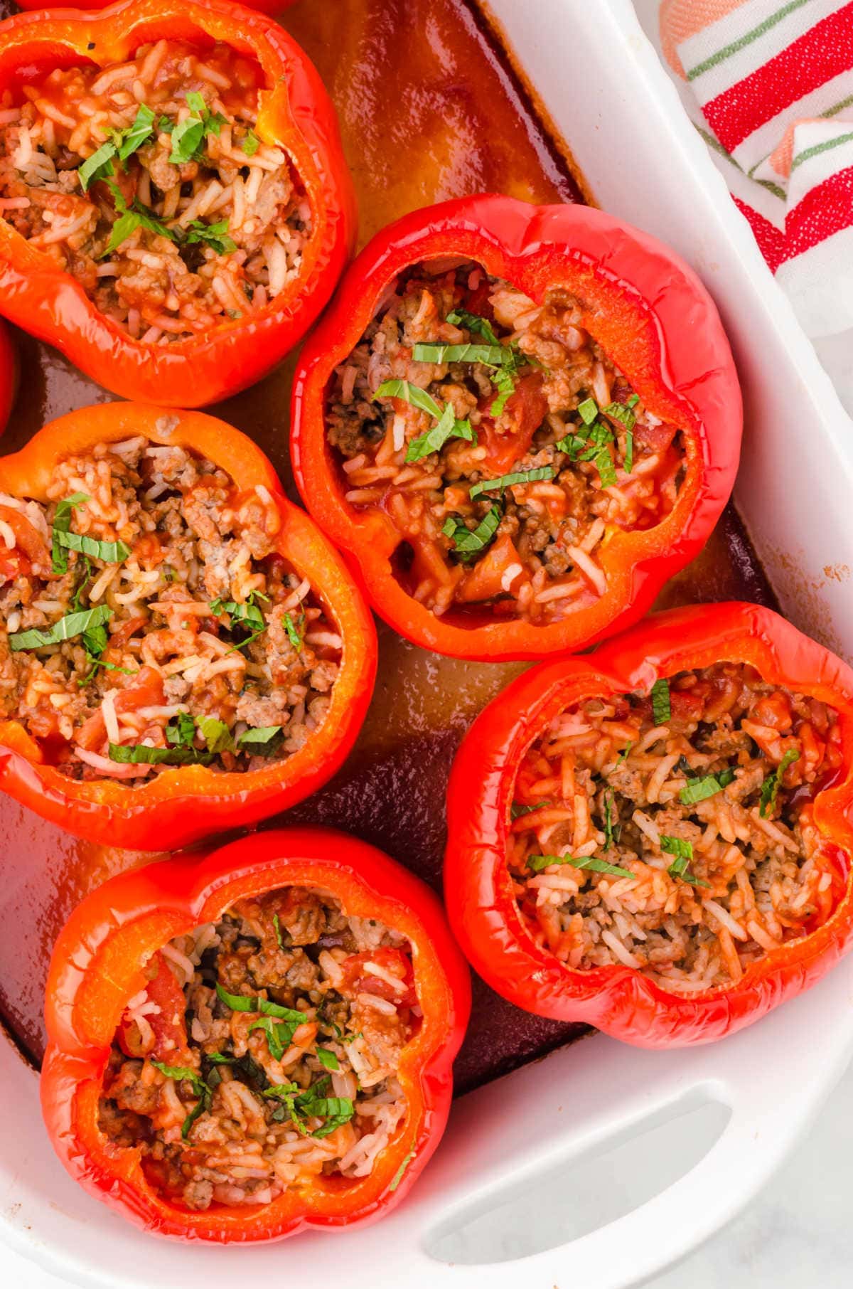 Overhead view of stuffed peppers sitting in tomato sauce in a white baking dish.
