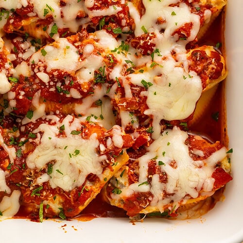 Close up of tomato and beef stuffed shells in a white baking dish topped with melted shredded cheese.