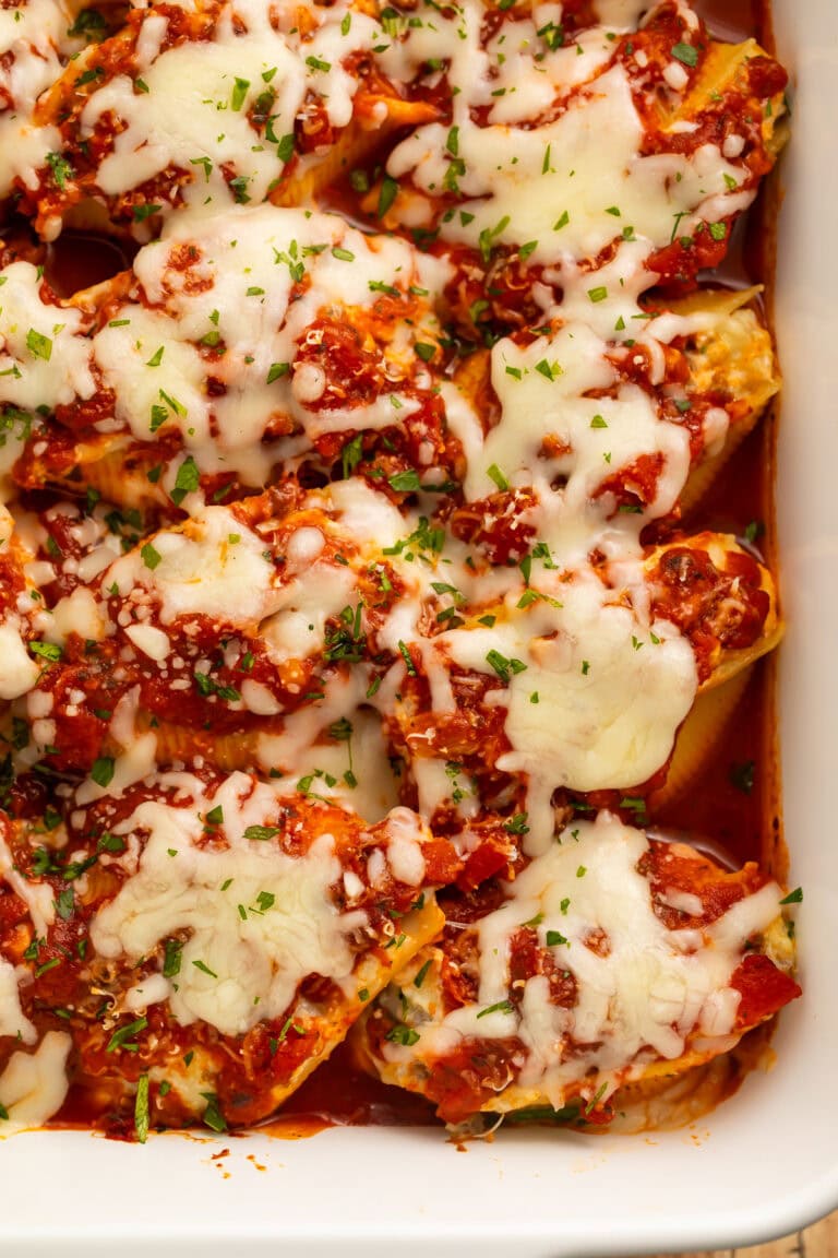 Close up of tomato and beef stuffed shells in a white baking dish topped with melted shredded cheese.