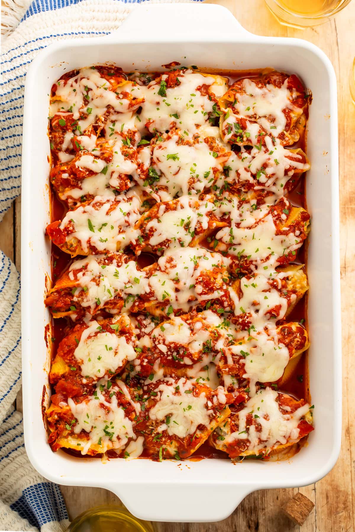 Overhead view of a white baking dish with three rows of stuffed shells topped with melted shredded cheese.