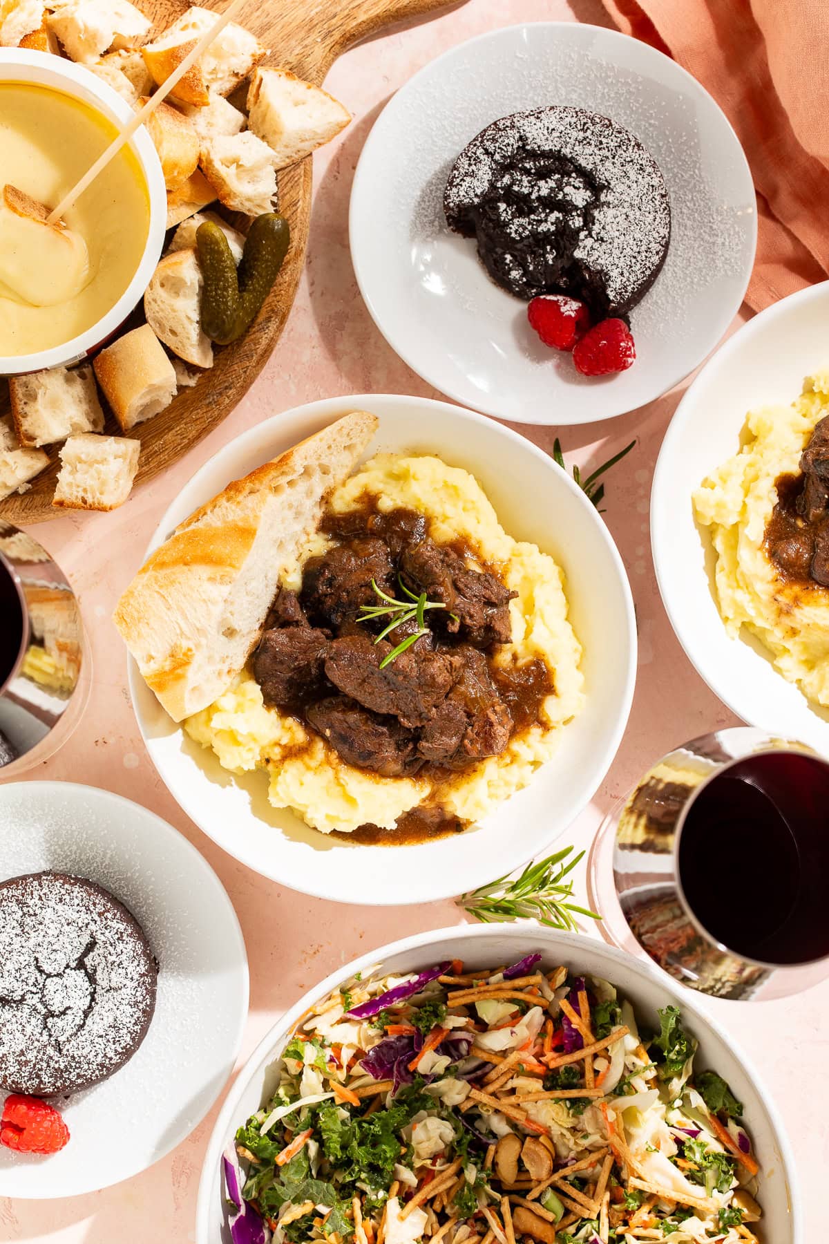 Overhead images of a Valentine's Day meal including braised short ribs with mashed potatoes, salad, fondu, and melt-in-the-middle chocolate puddings.