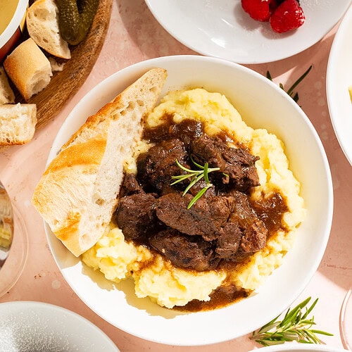 Close up of a Valentine's Day meal from Trader Joe's including braised short ribs with mashed potatoes, fondu with French bread, and chocolate fondants with fresh raspberries.